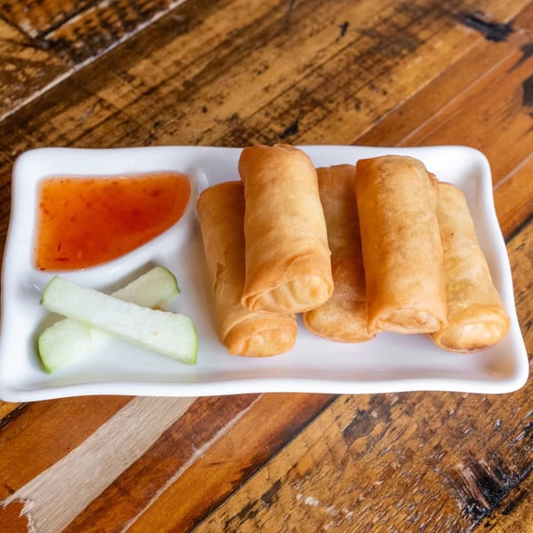 Crispy golden spring rolls with sweet chili sauce and cucumber slices on a white plate.