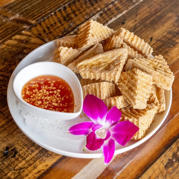 Crispy fried tofu triangles with sweet chili dipping sauce and a purple orchid on a white plate.