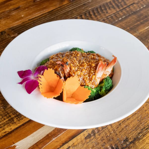 Siwa Thai Restaurant's shrimp dish with peanut sauce, broccoli, and decorative orchid on a white plate.