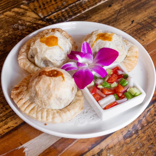 Three golden Thai curry puffs with a side of relish and a purple orchid on a white plate.