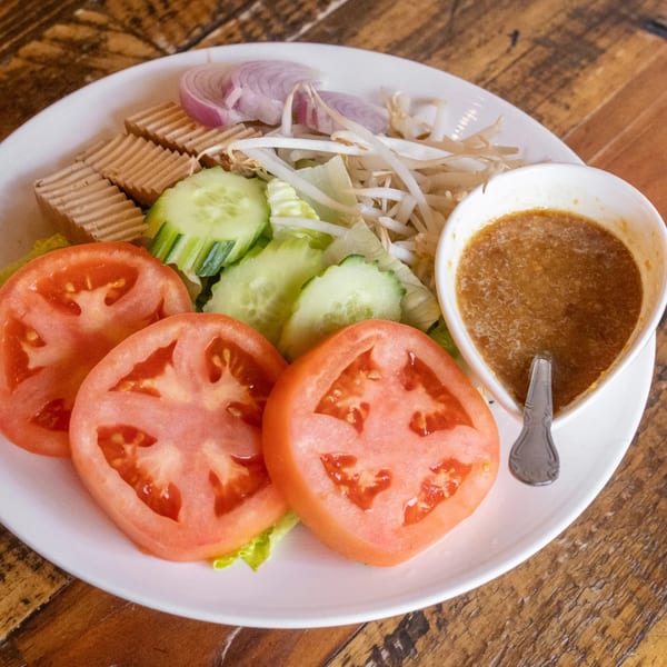 A Siwa Thai salad with sliced tomatoes, cucumbers, onions, tofu, bean sprouts, and peanut sauce.