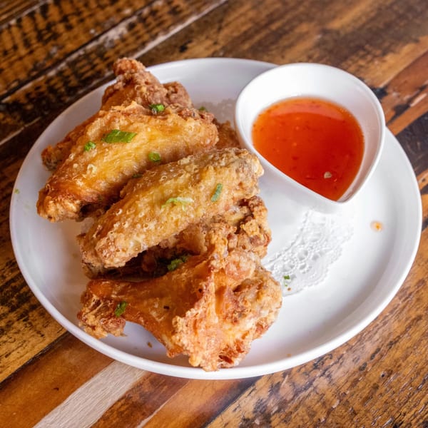 Crispy fried chicken wings with green onions and a side of sweet chili sauce on a white plate.
