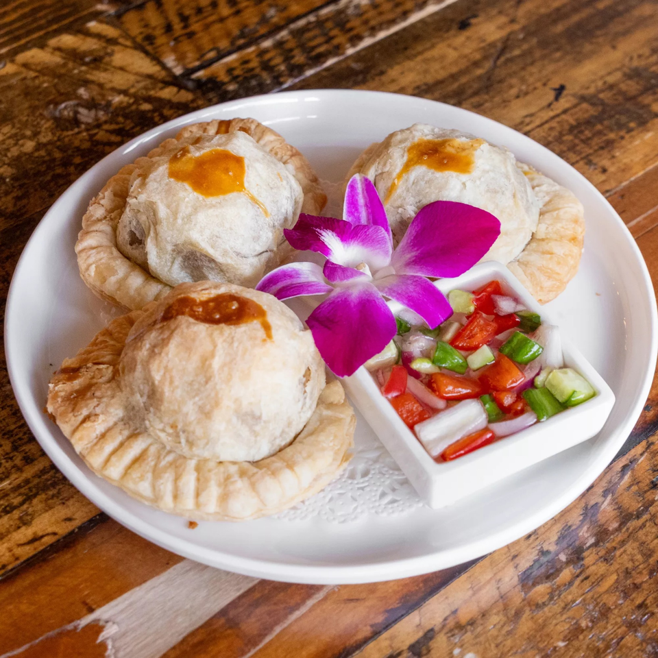 Three Thai curry puffs with a side of relish and a purple orchid on a white plate.